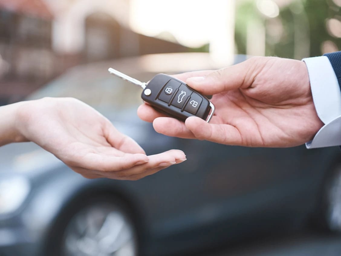 A person handing over a set of car keys in front of a car