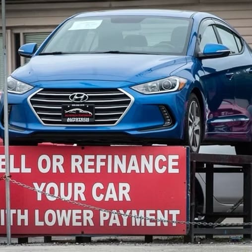 A car on a dealership lot above a sign reading 'Sell or refinance your car with lower payment'